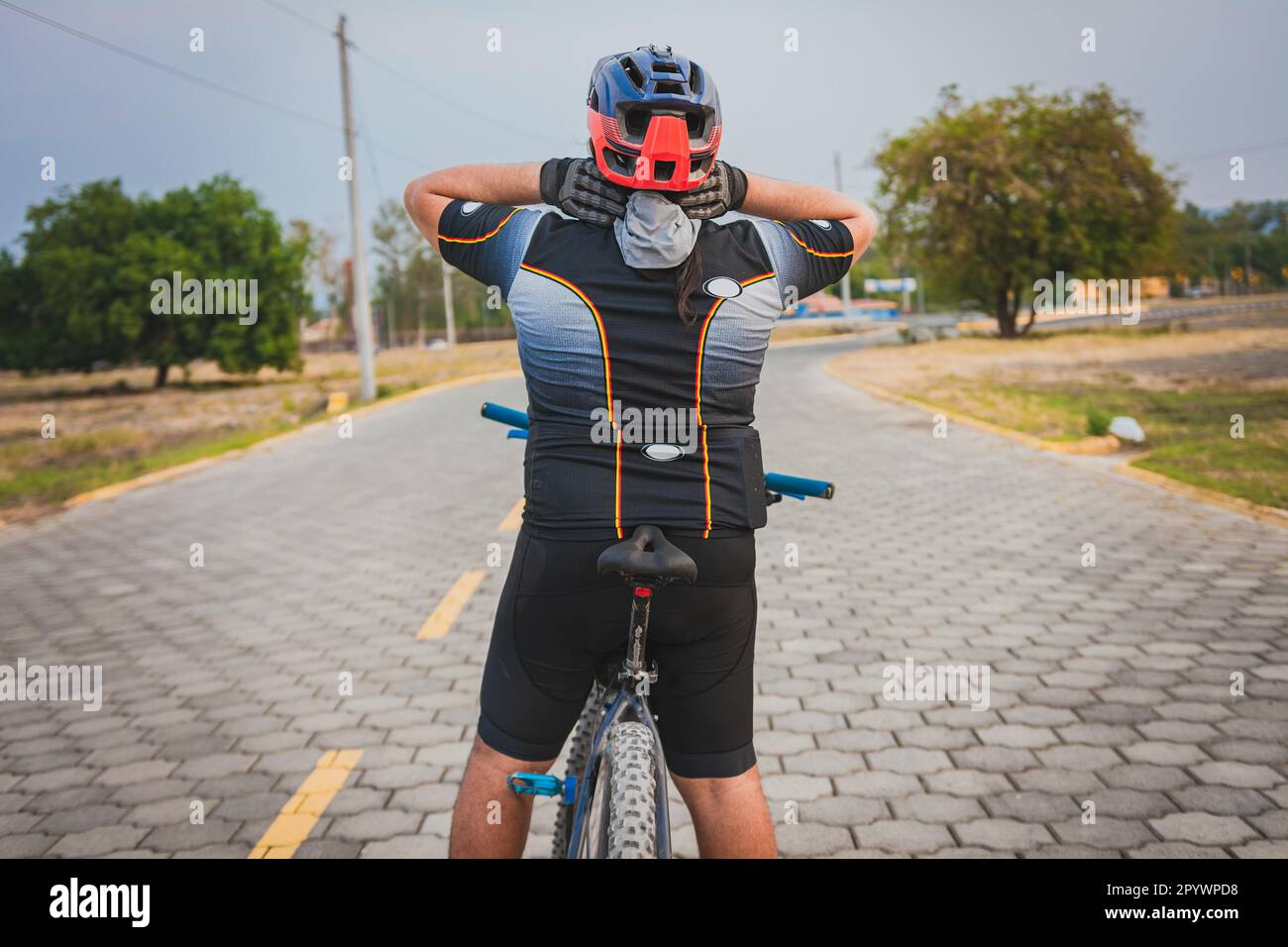 Rear view of a cyclist with neck pain with the bike. Back view of a cyclist man having neck pain