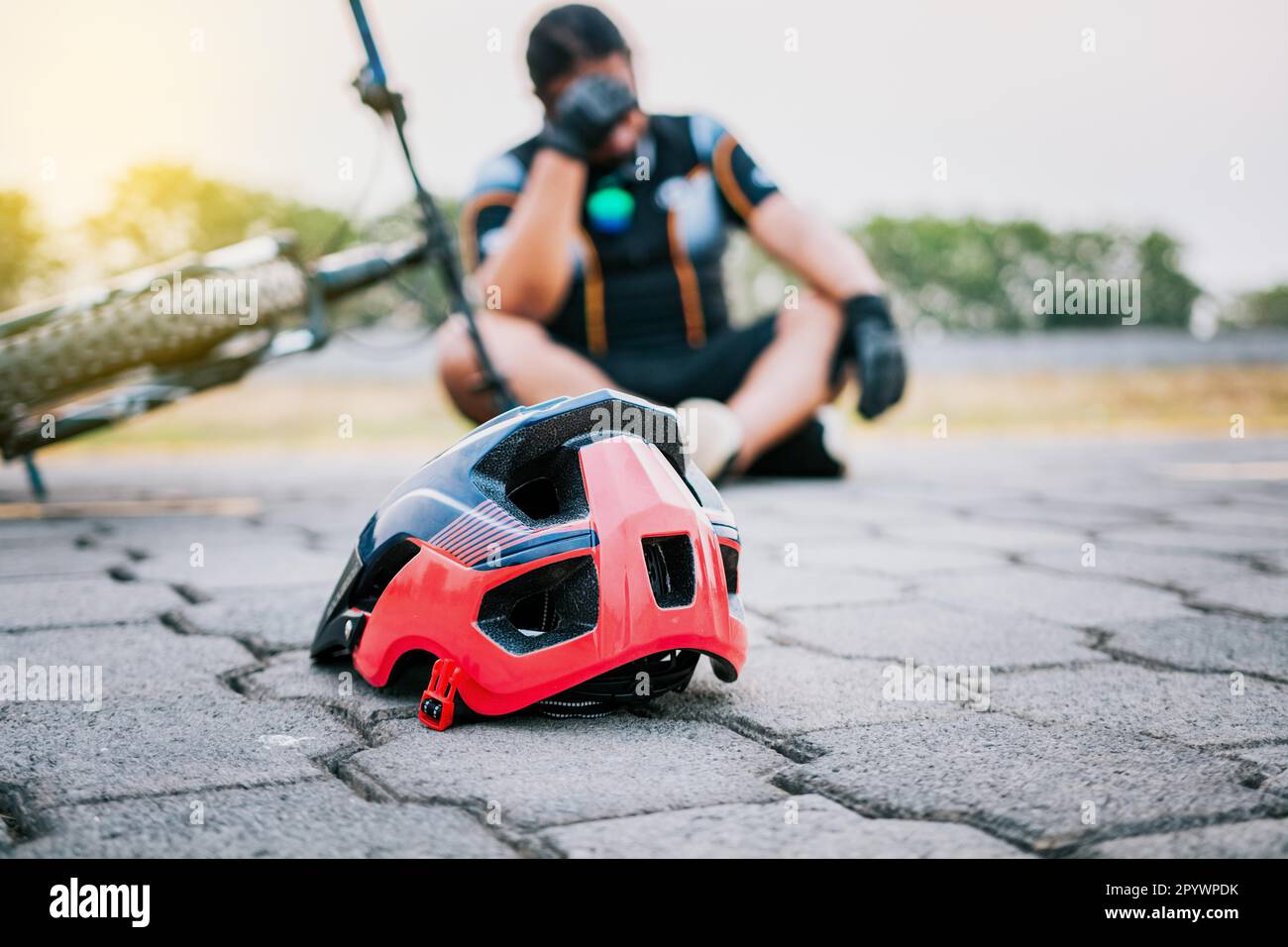 Accidented cyclist sitting on the pavement. Concept of crashed cyclist with helmet on the pavement in first focus Stock Photo