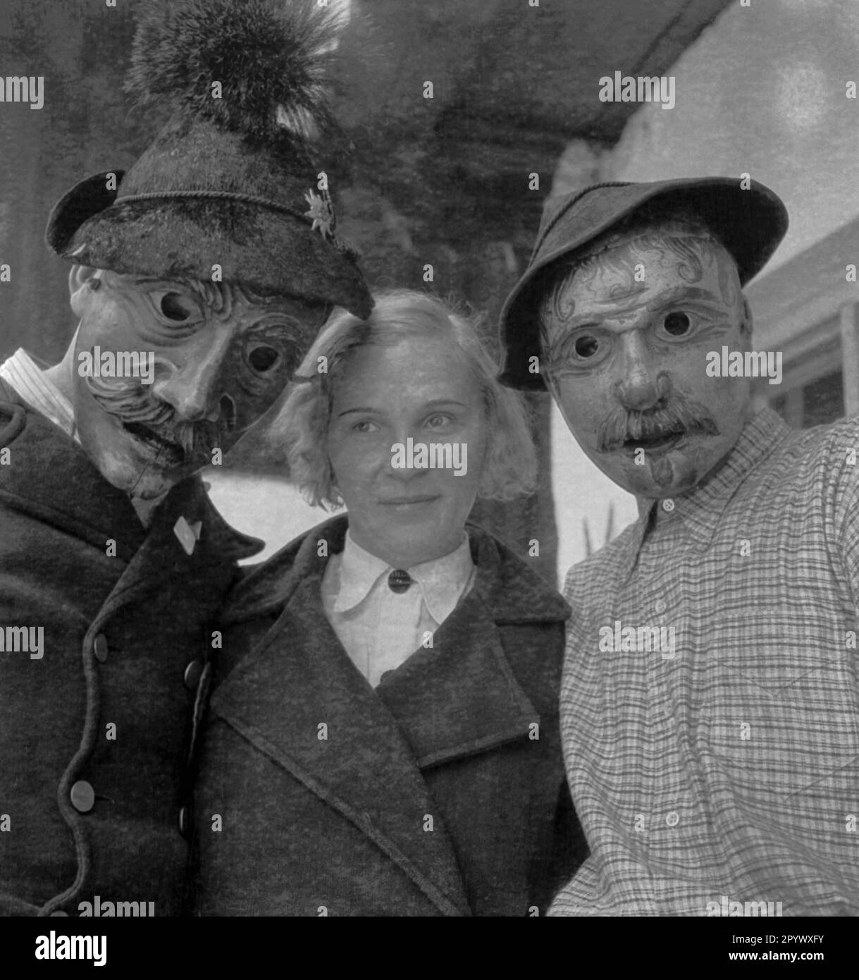 A woman between two men wearing hand-carved, ornate wooden masks (undated shot). Stock Photo