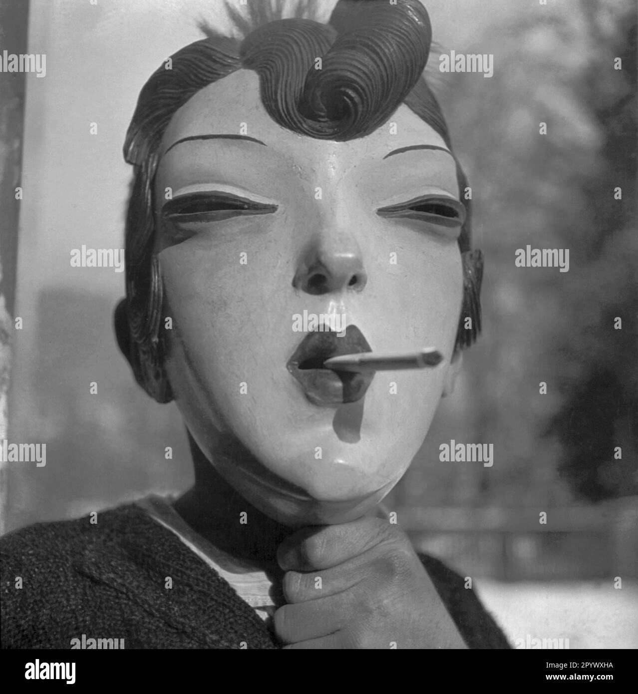 A person holds in front of her a hand-carved wooden mask showing a woman's face (undated shot). Stock Photo