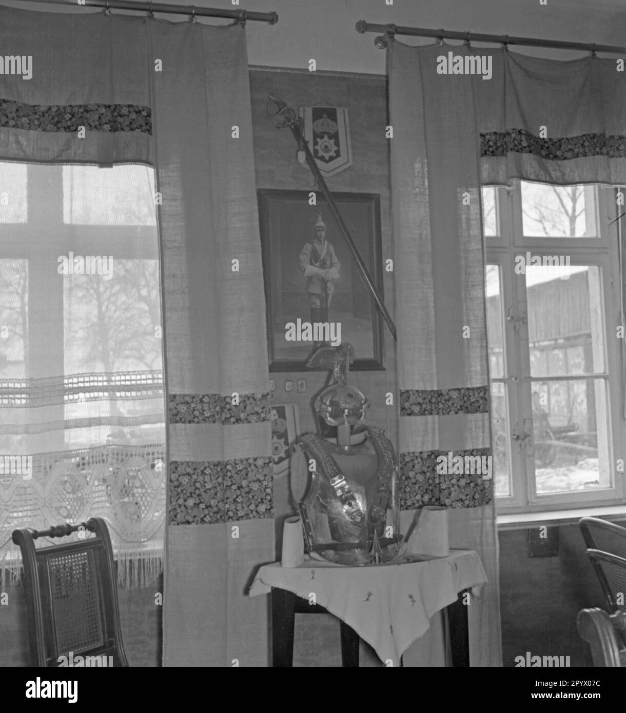 The chest protector and Adlerhelm (eagle helmet) of a cuirassier of the Gardes du Corps are set up on a table in the living room of a farmhouse. Above, hangs a photo of the cuirassier with his saber. Undated photo. Stock Photo