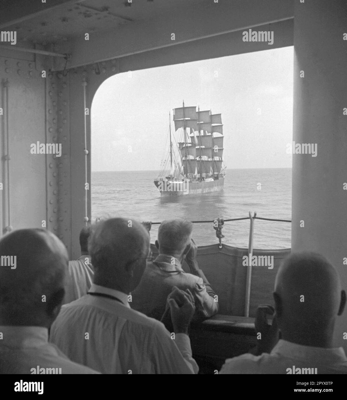 Older gentlemen look a tall ship with hoisted sails from aboard a large