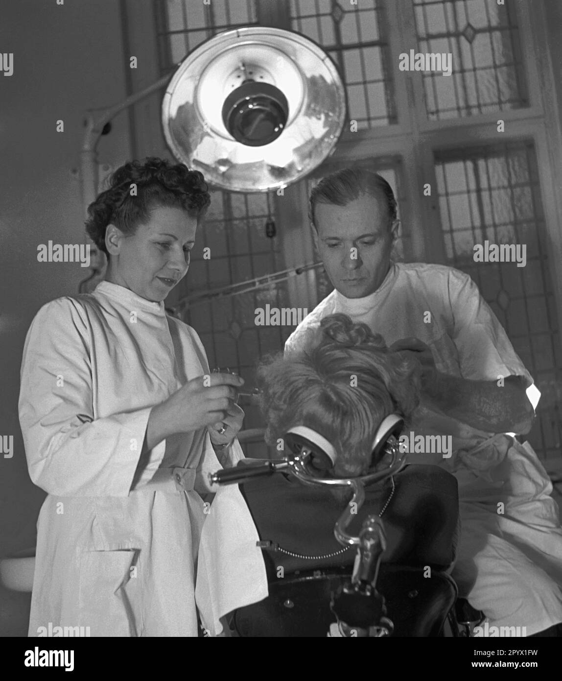 'Dentist Freese treats a patient. He is supported by a doctor. Scene from the series ''We work together''. The photographer accompanies couples in their respective occupations.' Stock Photo