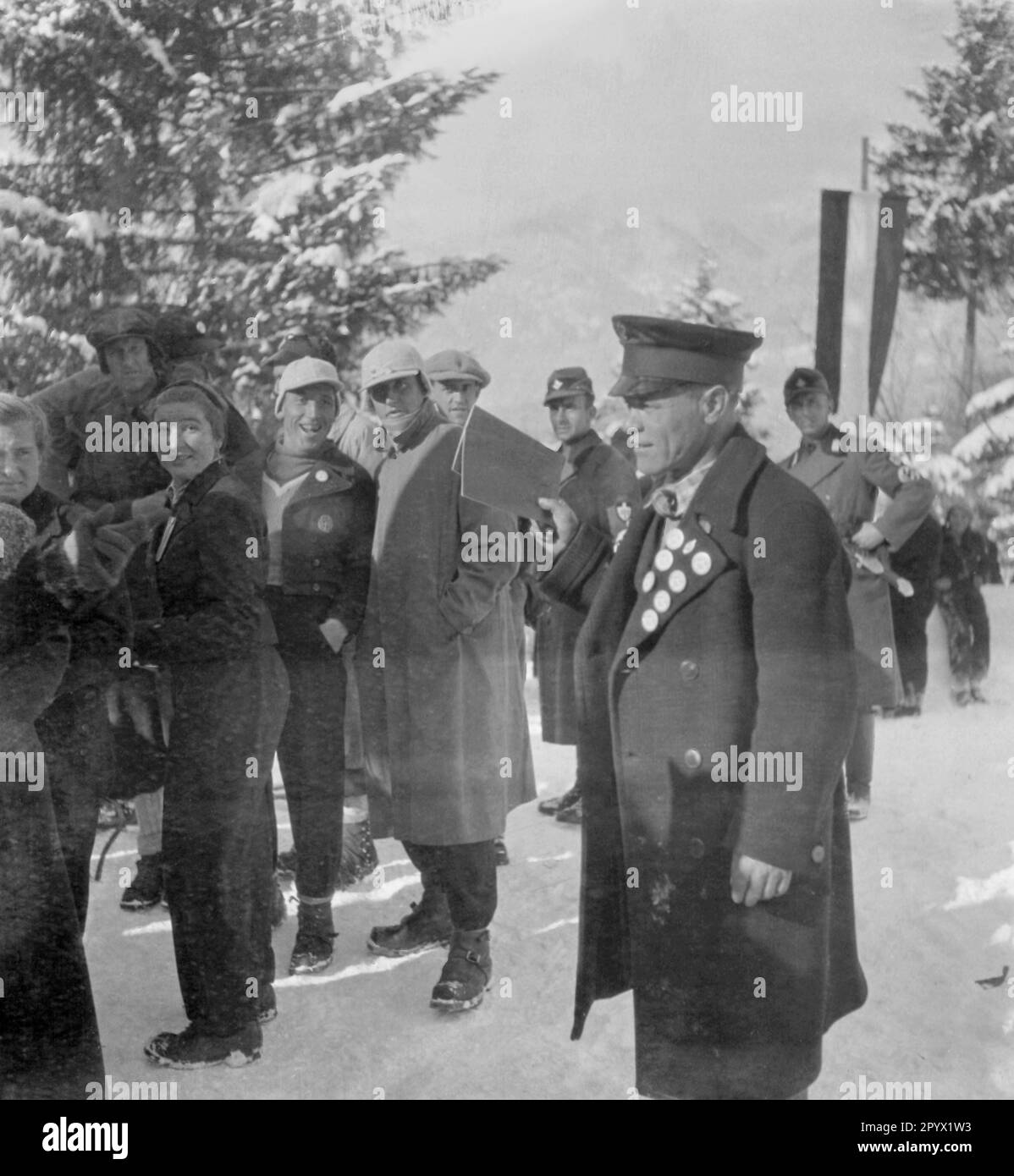 Athletes of the international tournament are waiting in line. Behind them are German soldiers. Undated photo, probably in the winter of 1933/1934. Stock Photo