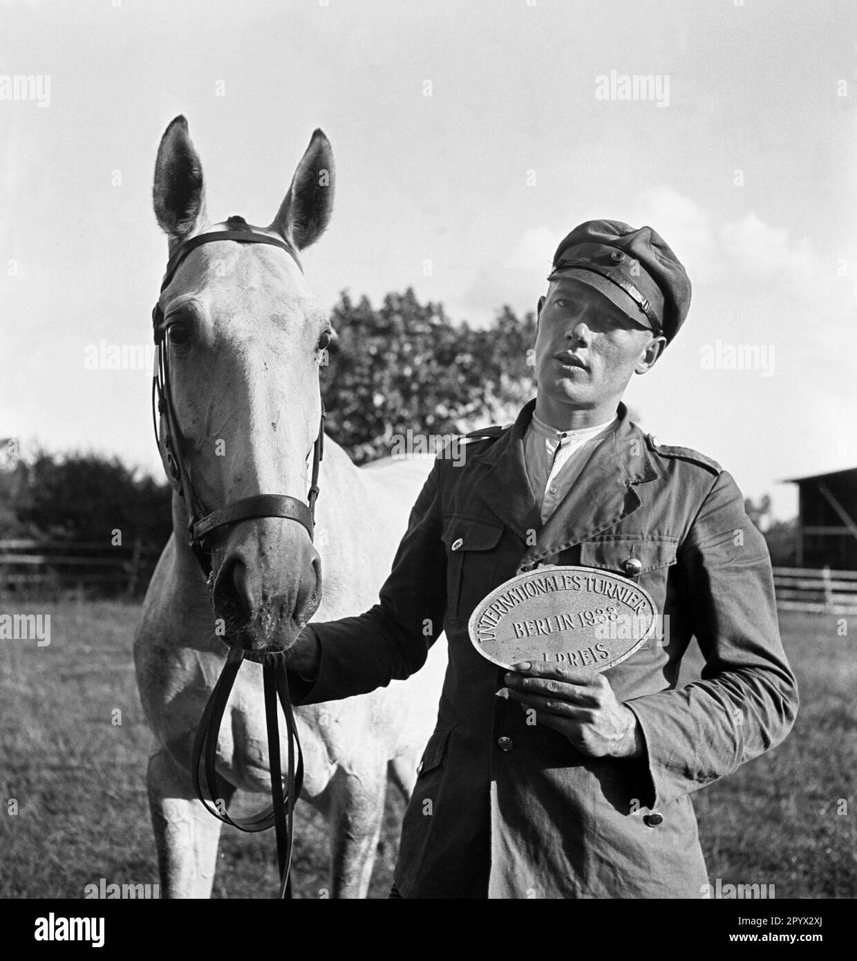 'The stud farm ''Broock'' in the district of Demmin (Pommern): A man presents his medal with the inscription: ''International Tournament, Berlin 1933, 1st Prize''. He is probably the show jumper who keeps his horse on a leash with his other hand.' Stock Photo