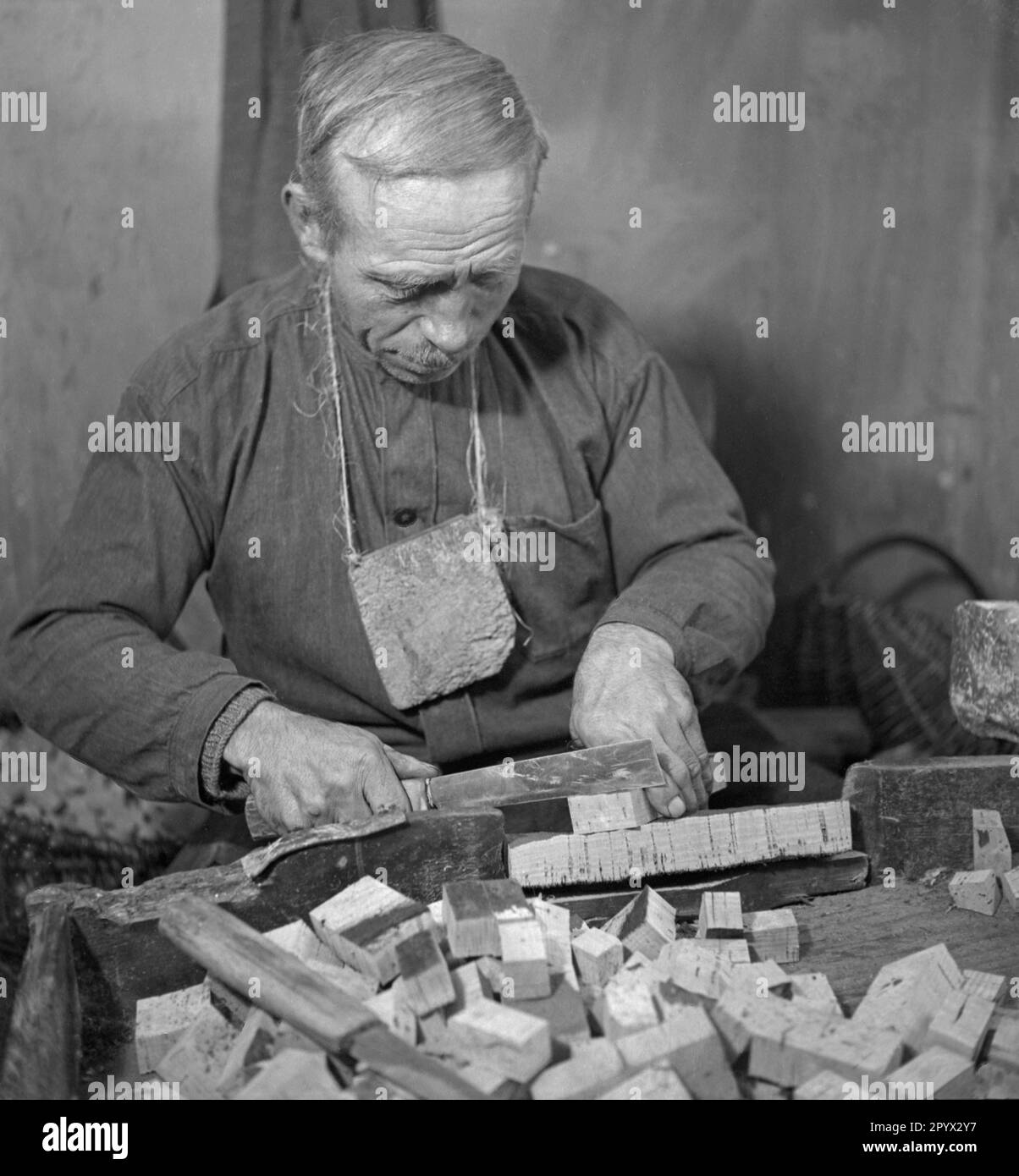 An elderly man cuts cork boards into smaller pieces. Undated photo