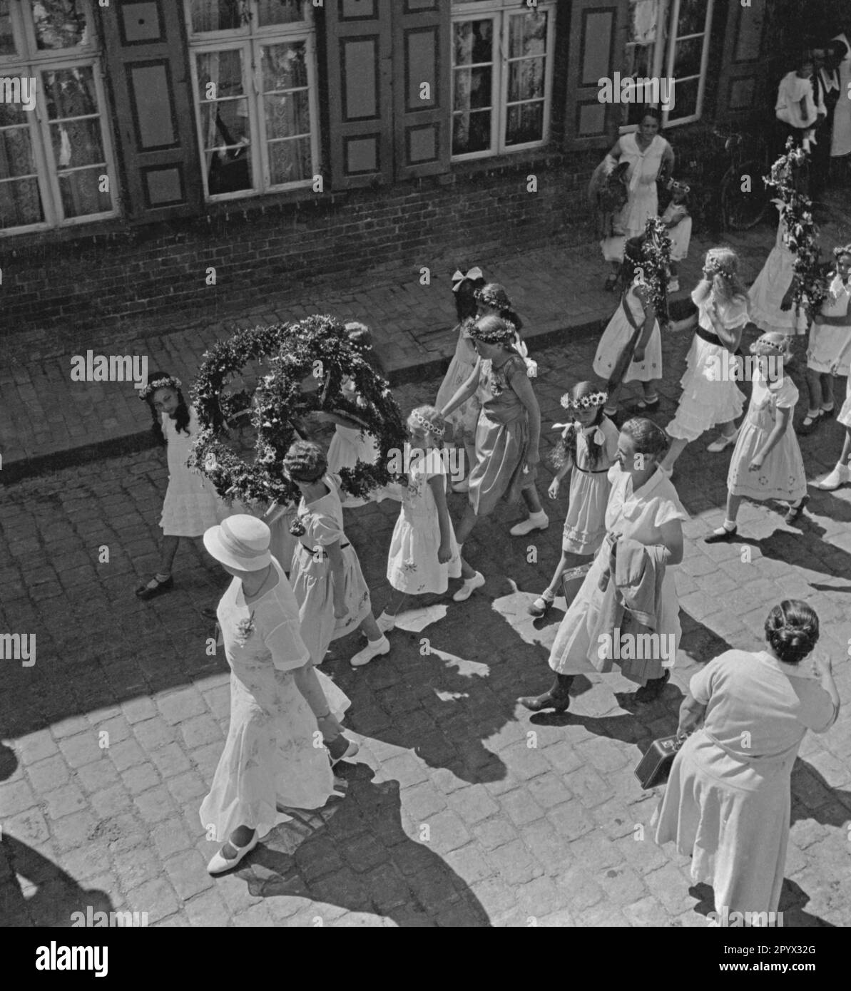During the children's festival in in Plau in Mecklenburg, some children, accompanied by adults, take part in a parade through the streets of the city. Here, several girls in a pageant with flower wreaths and garlands (undated photo). Stock Photo