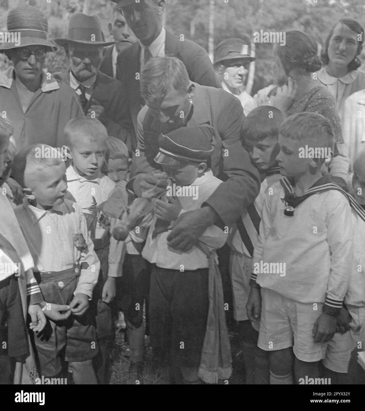 During the children's festival in Plau in Mecklenburg, a child with a cap gets a wooden bird attached to a string from a man. Several children are watching the happenings (undated photo). Stock Photo