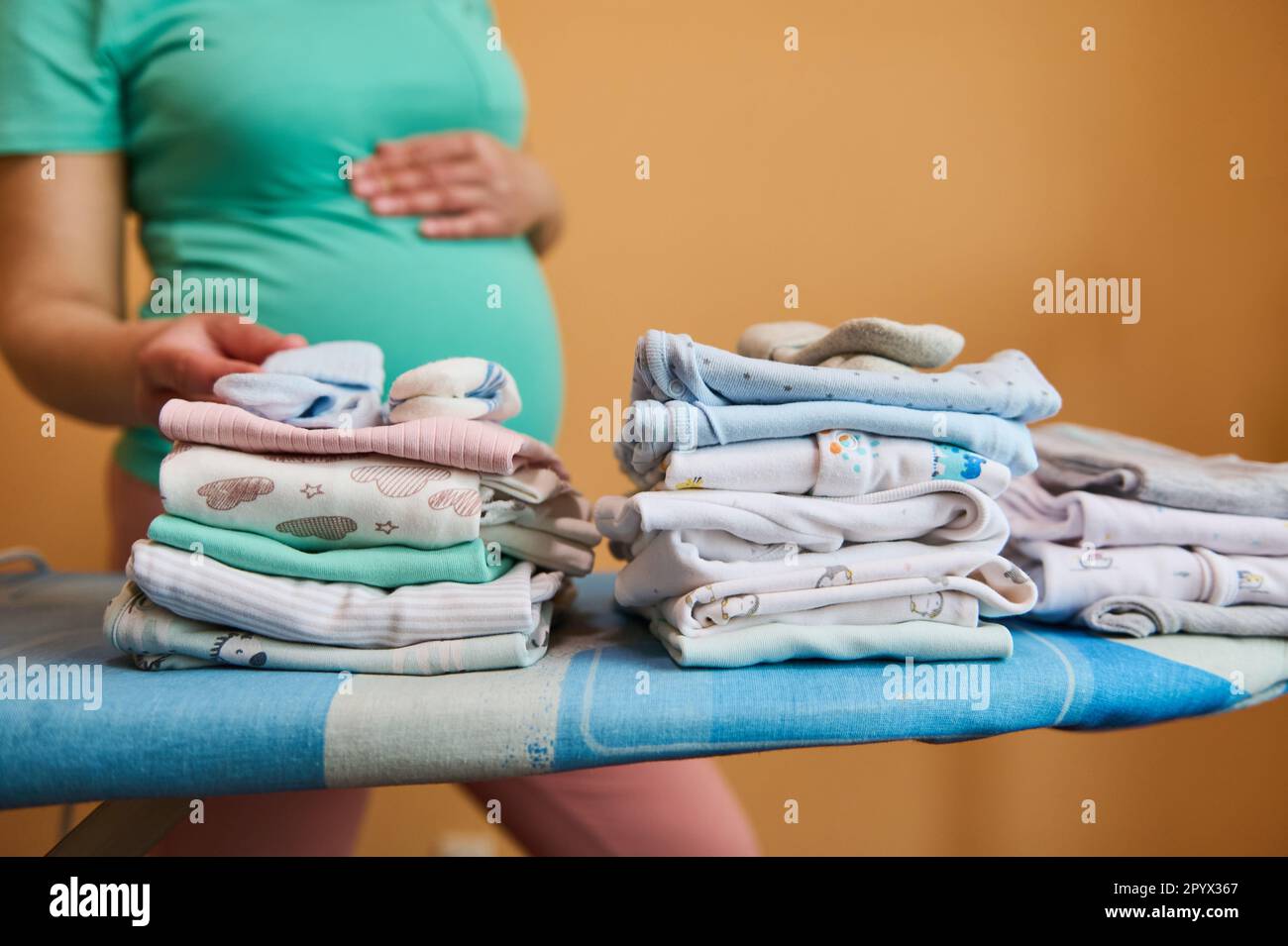 A stack of folded ironed clean baby clothes on ironing board, against a