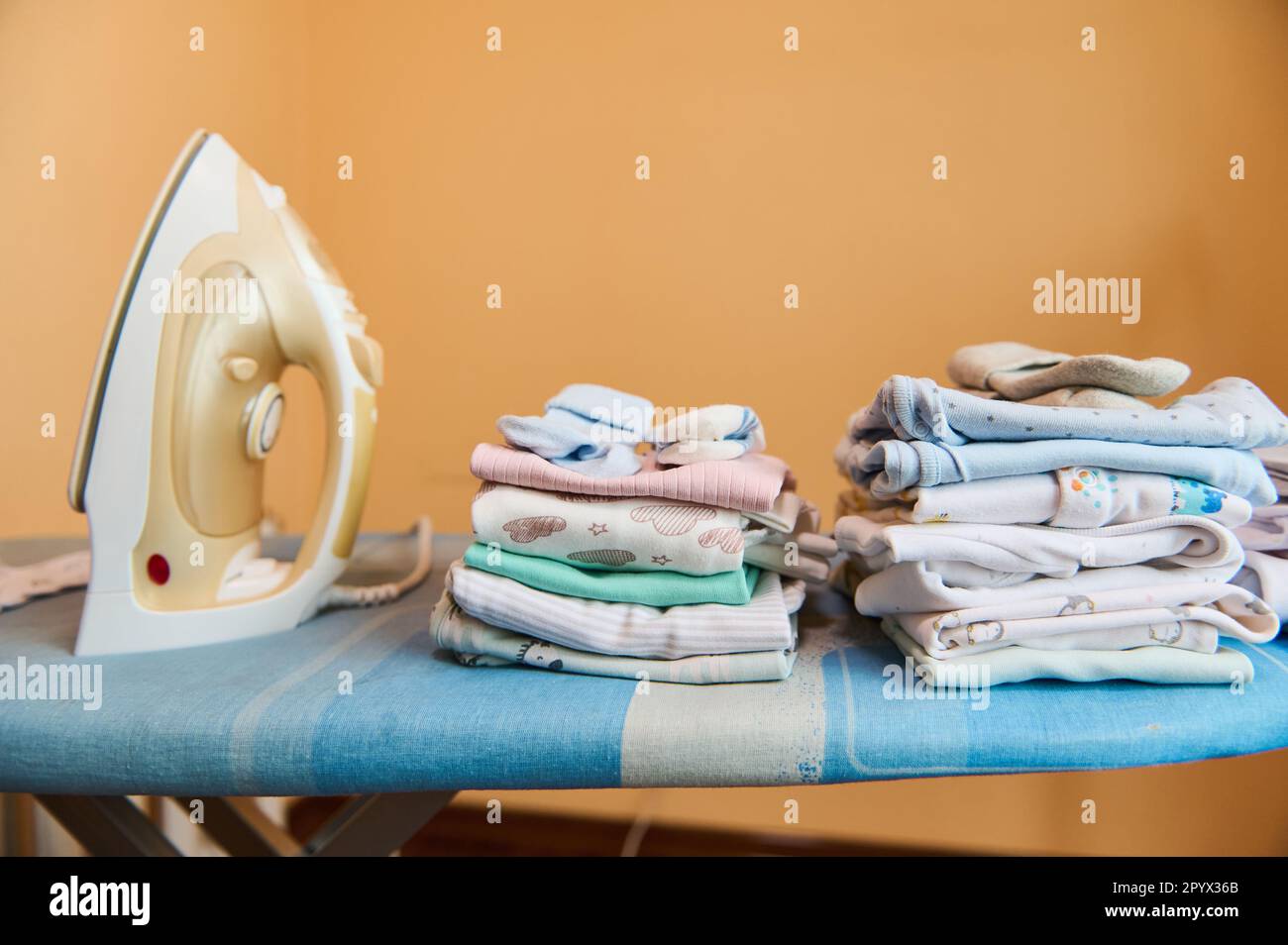 Still life electric steam iron and clean ironed newborn bodysuits