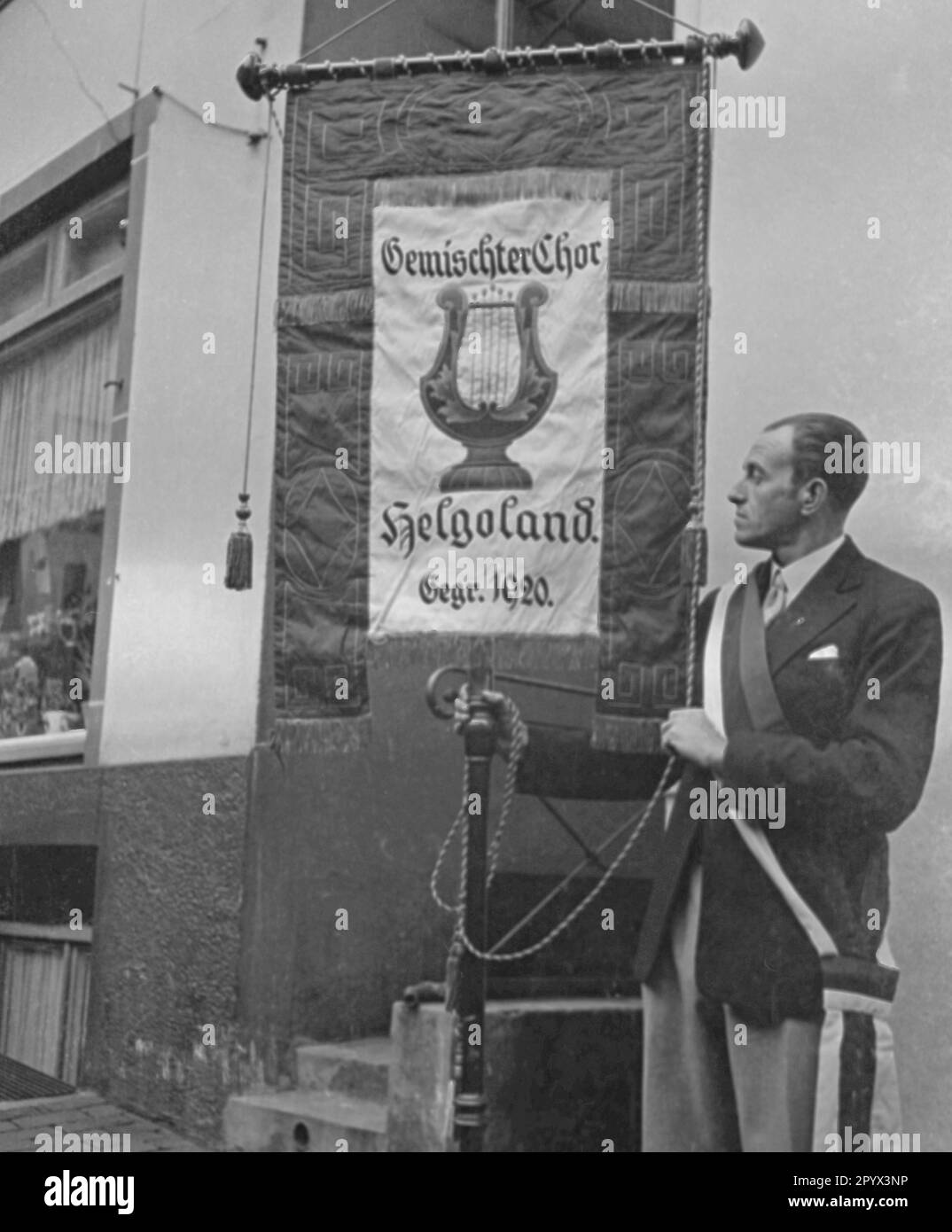 A man in full dress carries a banner of the Gemischter Chor Helgoland ...