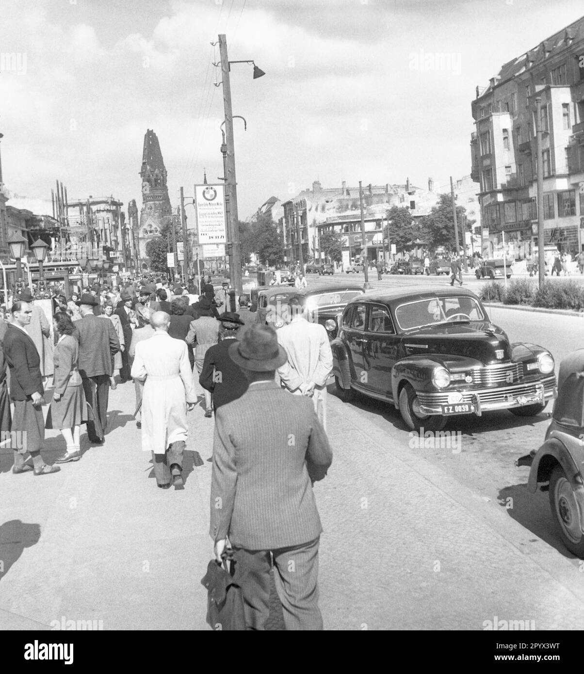 Undated photo of a sidewalk with flaneurs and buyers 1950 at the Kurfuerstendamm, British occupation zone, West Berlin, 1950. To the right and left of the street, partially destroyed facades. On the makeshift wooden lantern in the middle, an attached promotional poster of the Bavarian Motor Works. In the background, the ruined tower (Hohler Zahn) of the Kaiser Wilhelm Memorial Church. Stock Photo