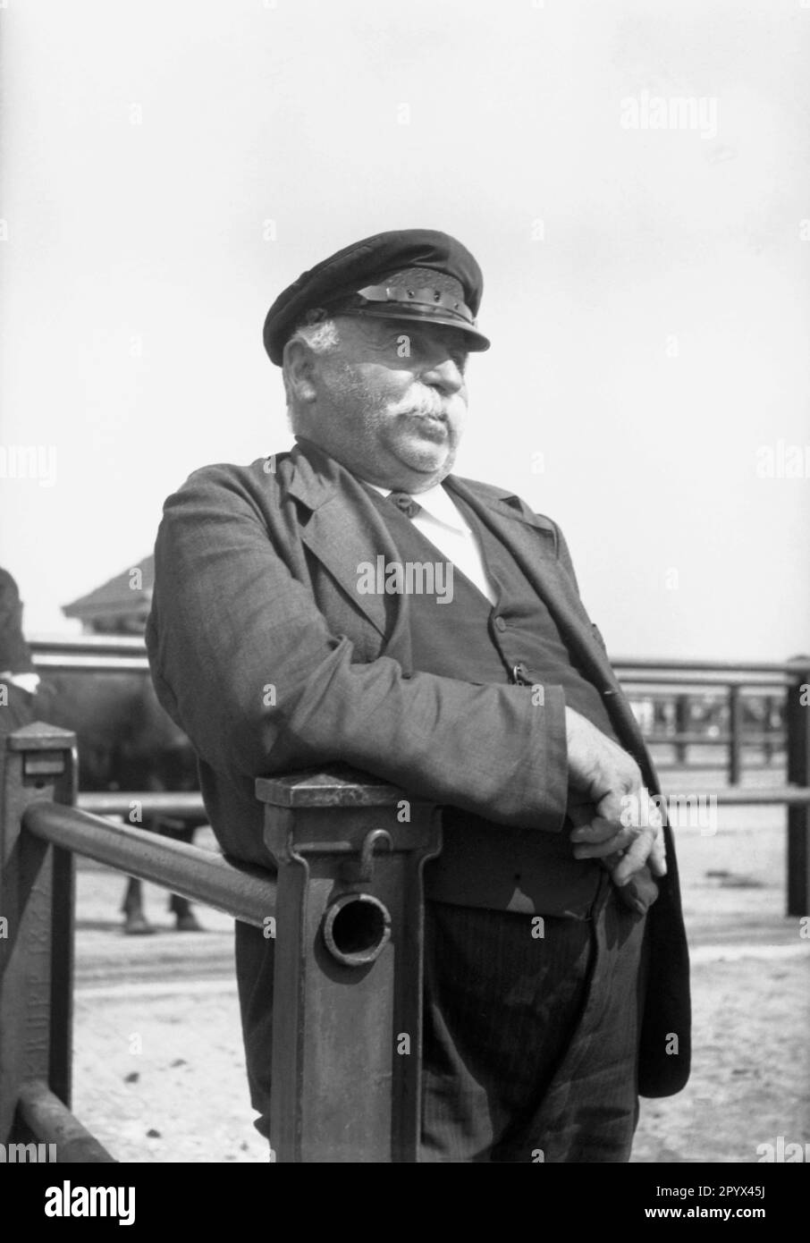 Undated photo of a farmer wearing a peaked cap (leaning on a gate) at the cattle market in Husum around 1940. Stock Photo