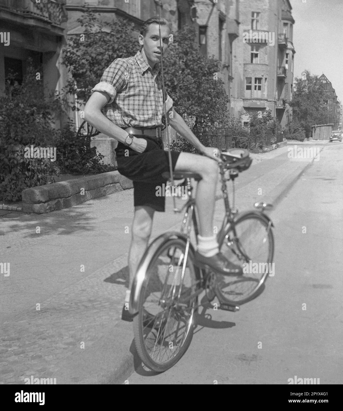 Undated photo of a cyclist in shorts and plaid shirt riding a men's bike equipped with an antenna and a transistor radio in West Berlin. Stock Photo