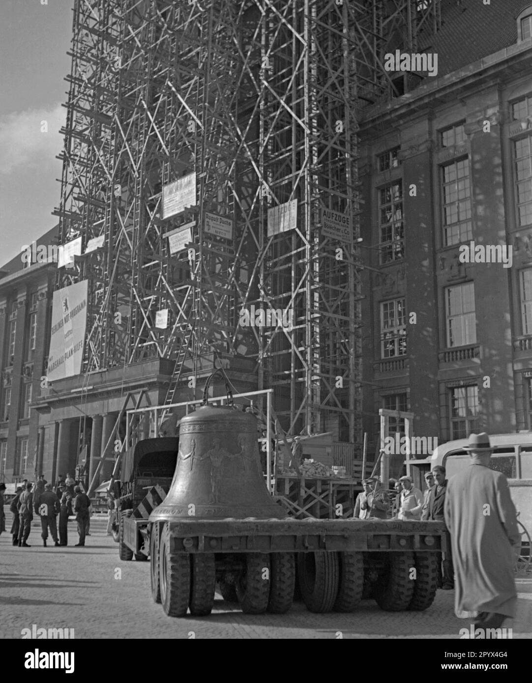 Photo of the Freedom Bell on the back of a low loader of the U.S. Army on Rathausplatz shortly before its installation in the tower of the seat of the Governing Mayor of Berlin, Ernst Reuter (1948-1953) on October 21, 1950. On the right, construction workers in white coats. On the right side of the truck, American soldiers in front of the columned doorway. In the background, the scaffolded tower and the partially destroyed facade of the building. On the scaffold, a poster of the American occupation force (inscription: Emergency Programme of Berlin with European Recovery Program). The bell Stock Photo