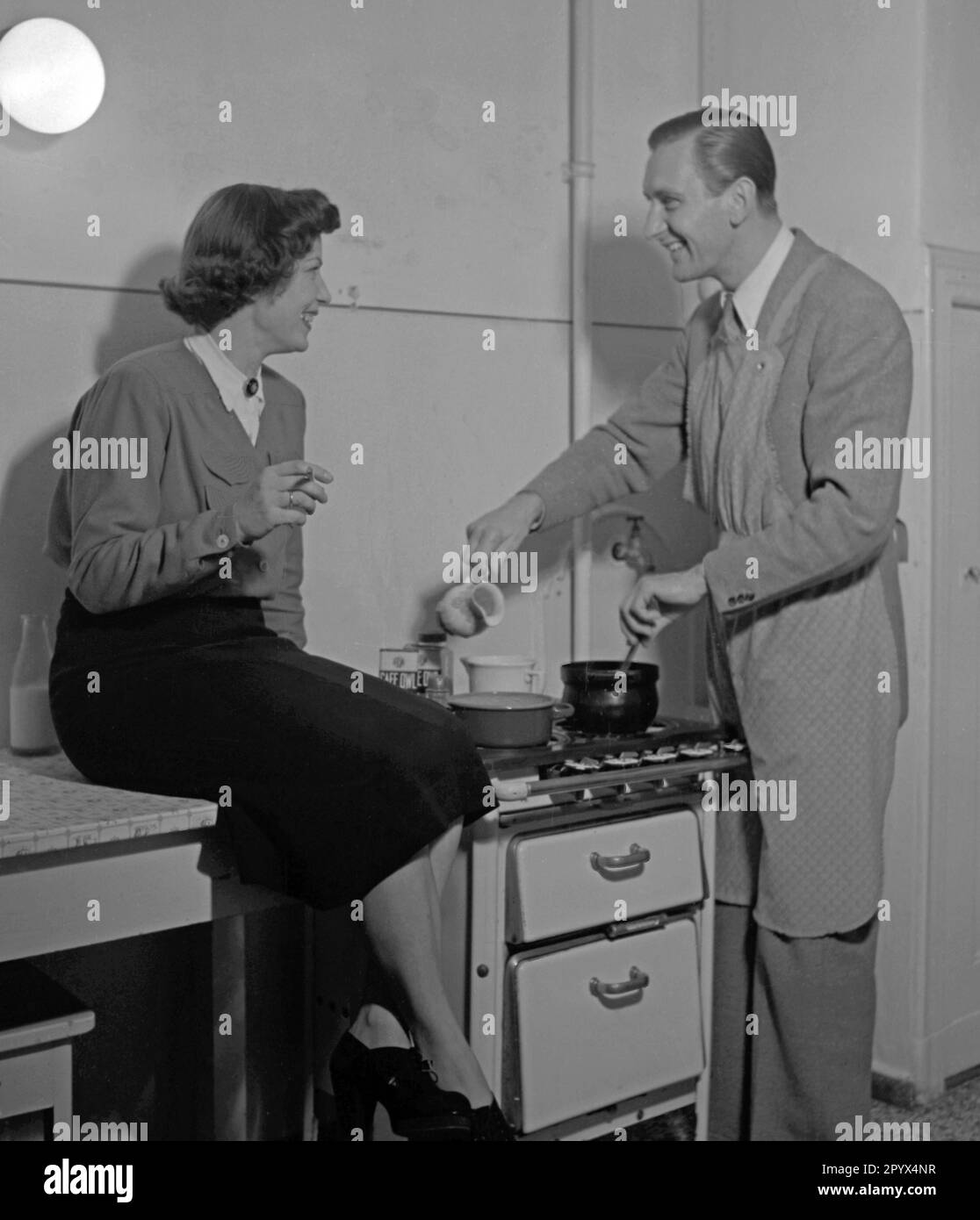 A man flirts with a woman in the kitchen. Undated picture, probably from the year 1950. Stock Photo