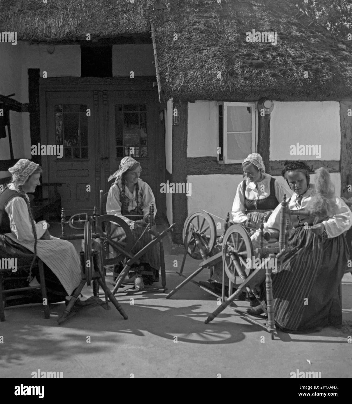 Women spin on spinning wheels in a village on the Baltic coast in