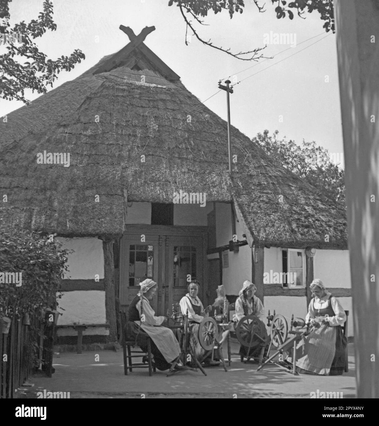 Women spin on spinning wheels in a village on the Baltic coast in