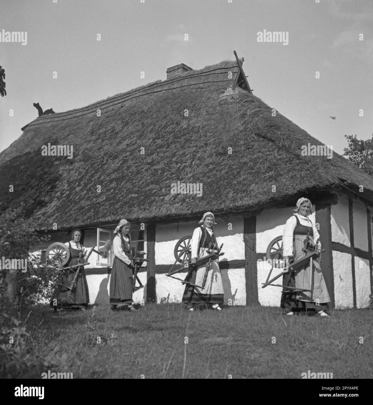 Women carry their spinning wheels through a village on the Baltic coast
