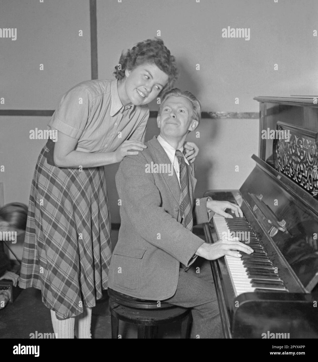 A man plays a piece of music on the piano to a woman. Undated picture