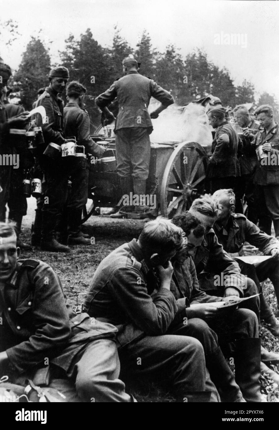 German soldiers reading a front newspaper during a break in the march. In the background, food is being served. Photo: Müller. [automated translation] Stock Photo