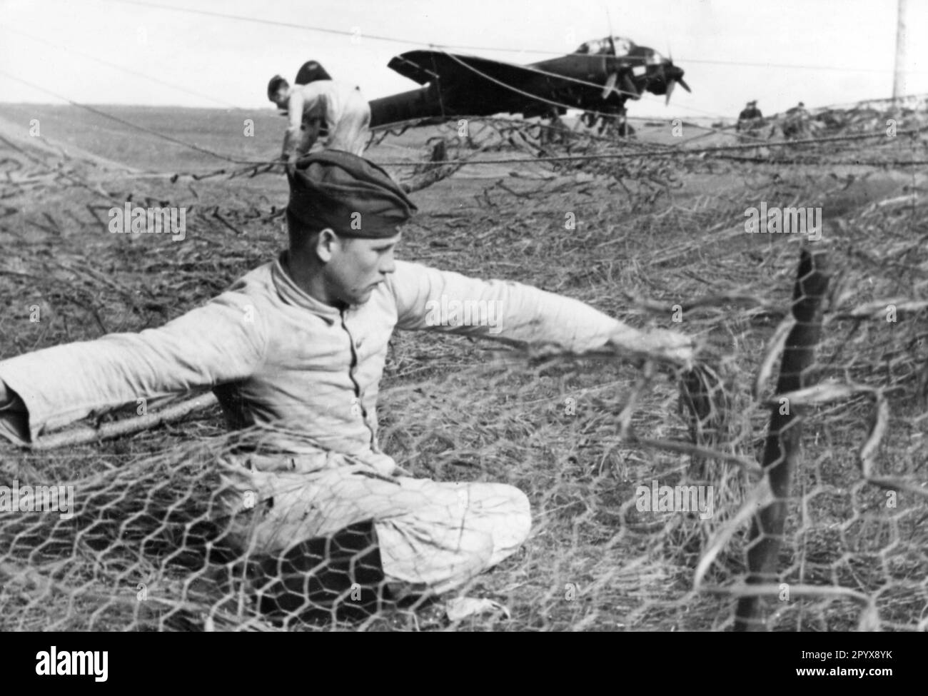 Members of a construction company build camouflaged boxes for Junkers Ju 88 Luftwaffe fighter planes. The wire mesh is covered with camouflage material to conceal the planes from reconnaissance during the day on the field airfield. The aircraft in the background wears a dark coat of paint for night operations against the British Isles. Photo Göricke. [automated translation] Stock Photo