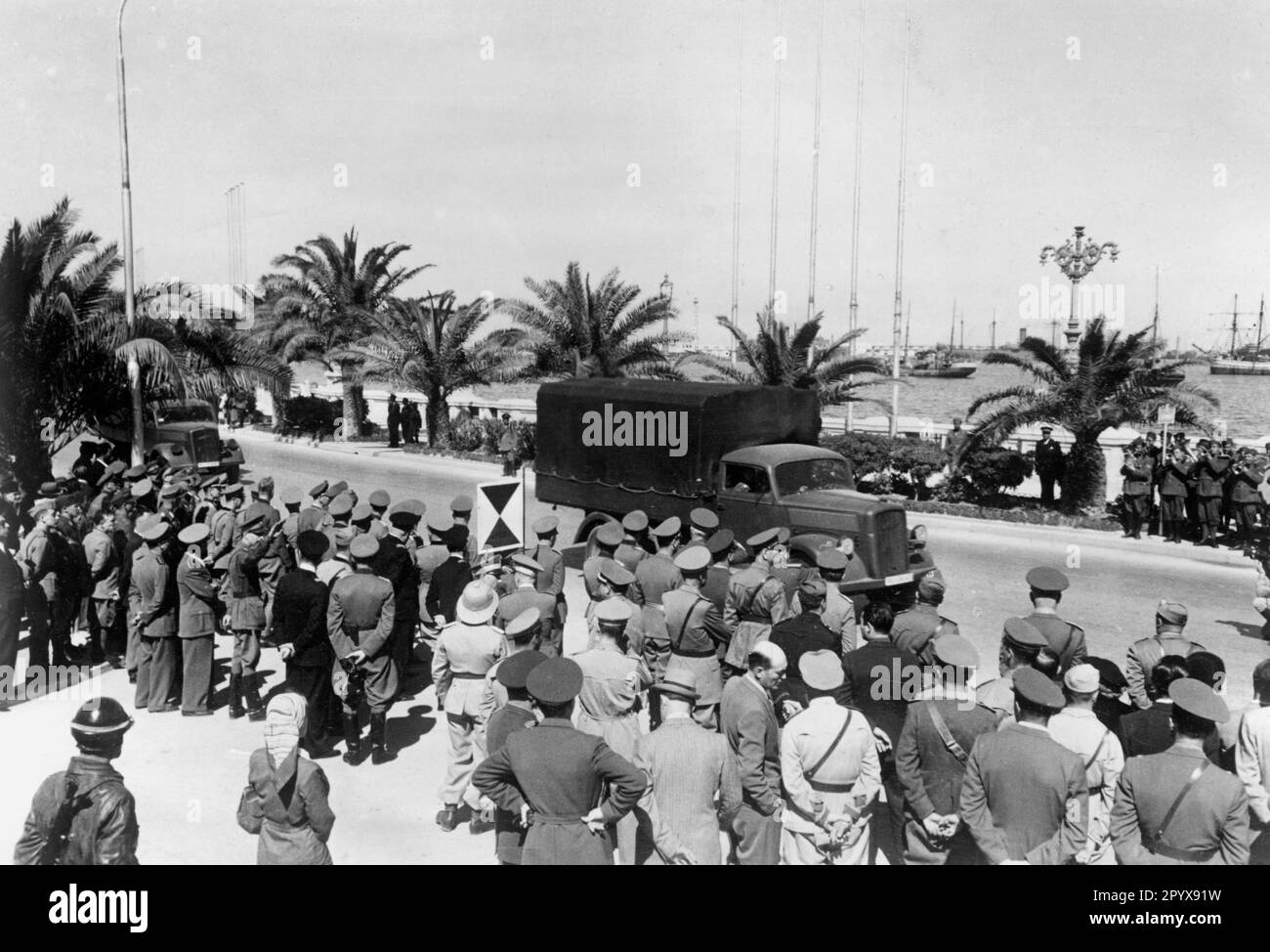 Truck Opel Blitz of the German Africa Corps in Tripoli surrounded by soldiers on a drive past Lieutenant General Erwin Rommel (in the group of officers). In the picture also the stander of the commanding general of a corps. Photo: Sturm [automated translation] Stock Photo