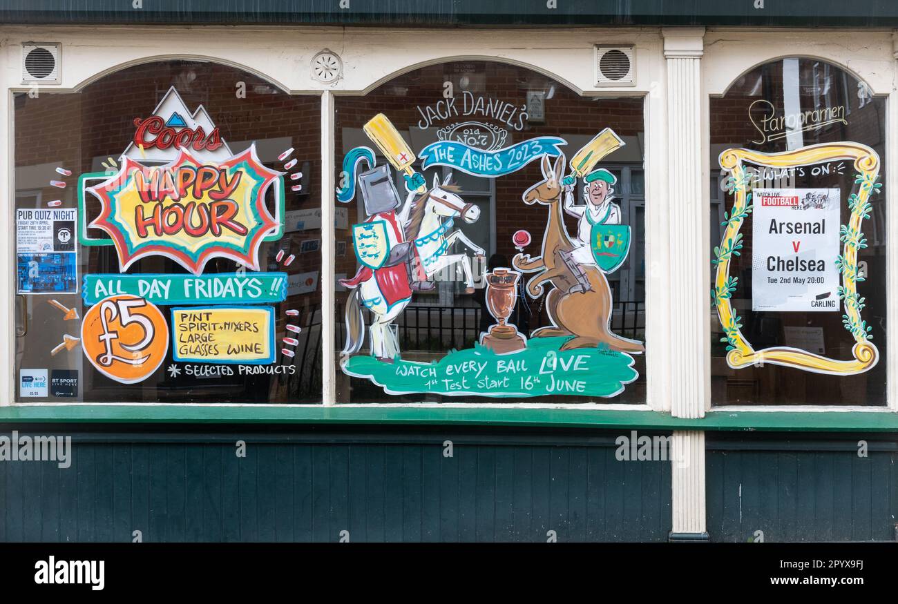 Painted decorated pub window advertising happy hour and sports events including The Ashes and football on TV, England, UK Stock Photo