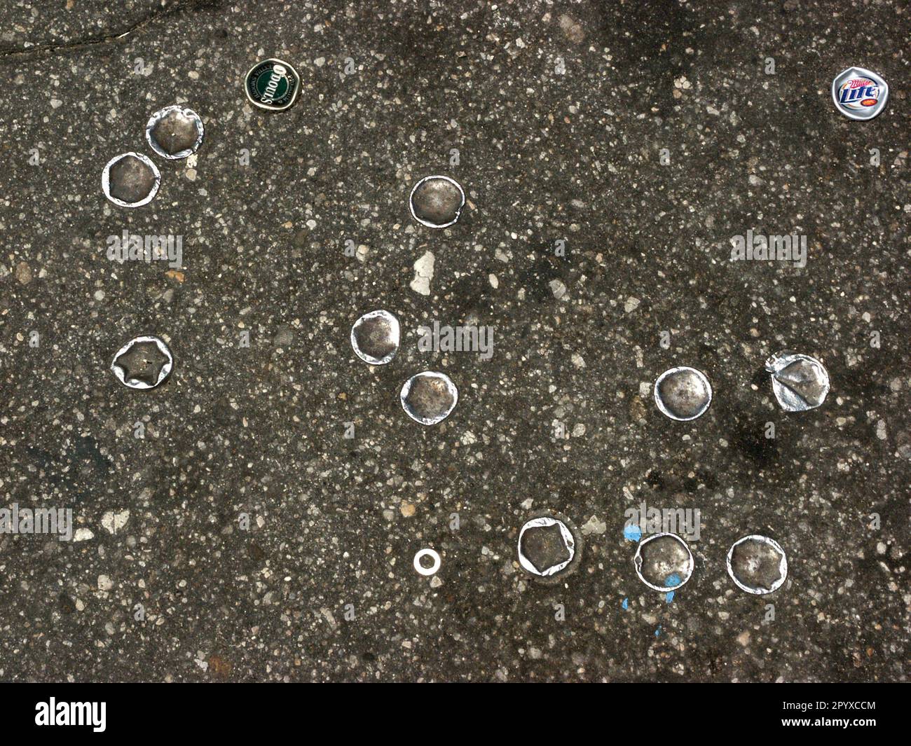Bottlecaps in front of a convenience store, flattened and embedded into pavement after being run over by vehicles. Stock Photo