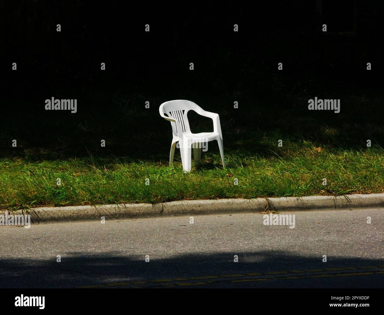 Empty white chair sits by a roadside. Stock Photo