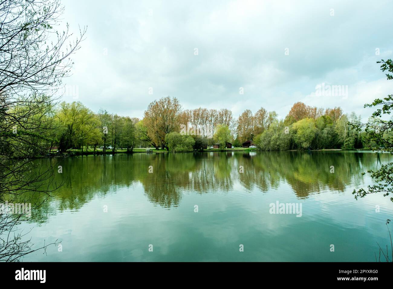 Fishing Lake Surrounded By Trees Reflected In The Calm Water Under A Grey Cloudy Sky Stock Photo