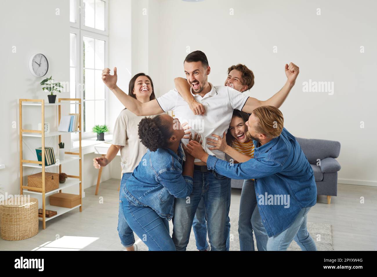 Group of excited young people congratulate friend man who's achieved great success. Stock Photo