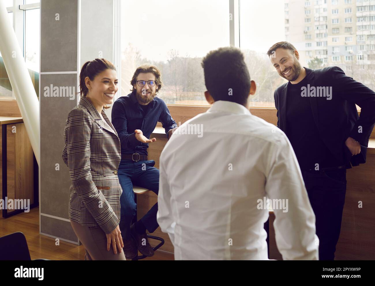 Collegues are talking in office during work break near the window, smiling and friendly people. Stock Photo