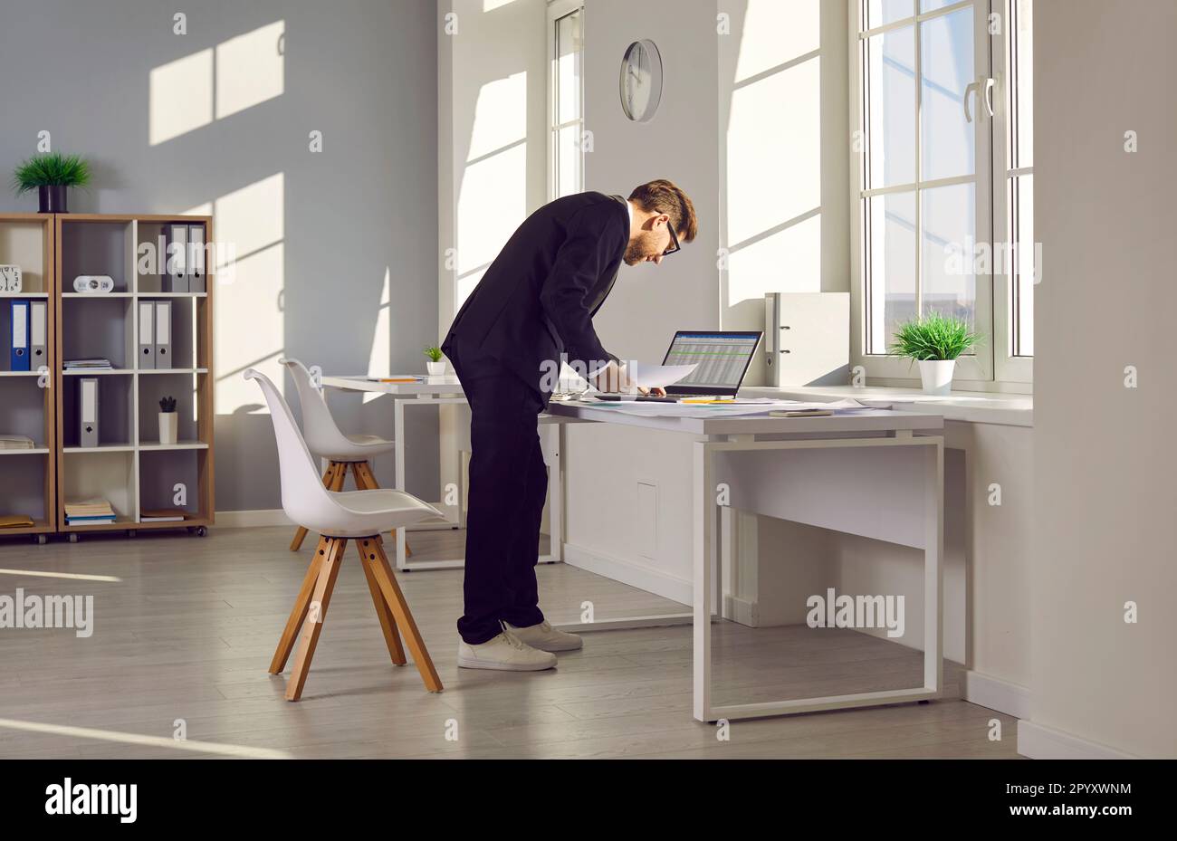 Accountant standing by his office desk, doing some paperwork, and using a laptop computer Stock Photo