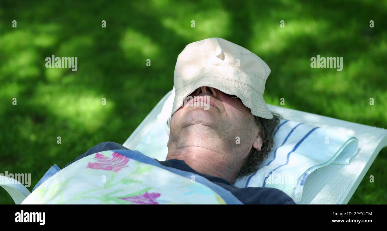 Older man napping outside covered by hat. Retired senior person