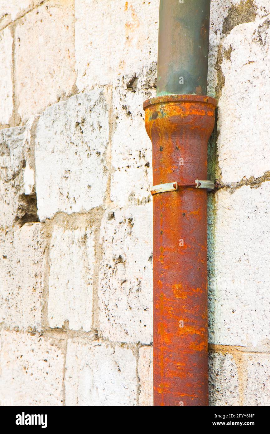 Old cast iron and copper downpipe against a stone wall (Italy Stock