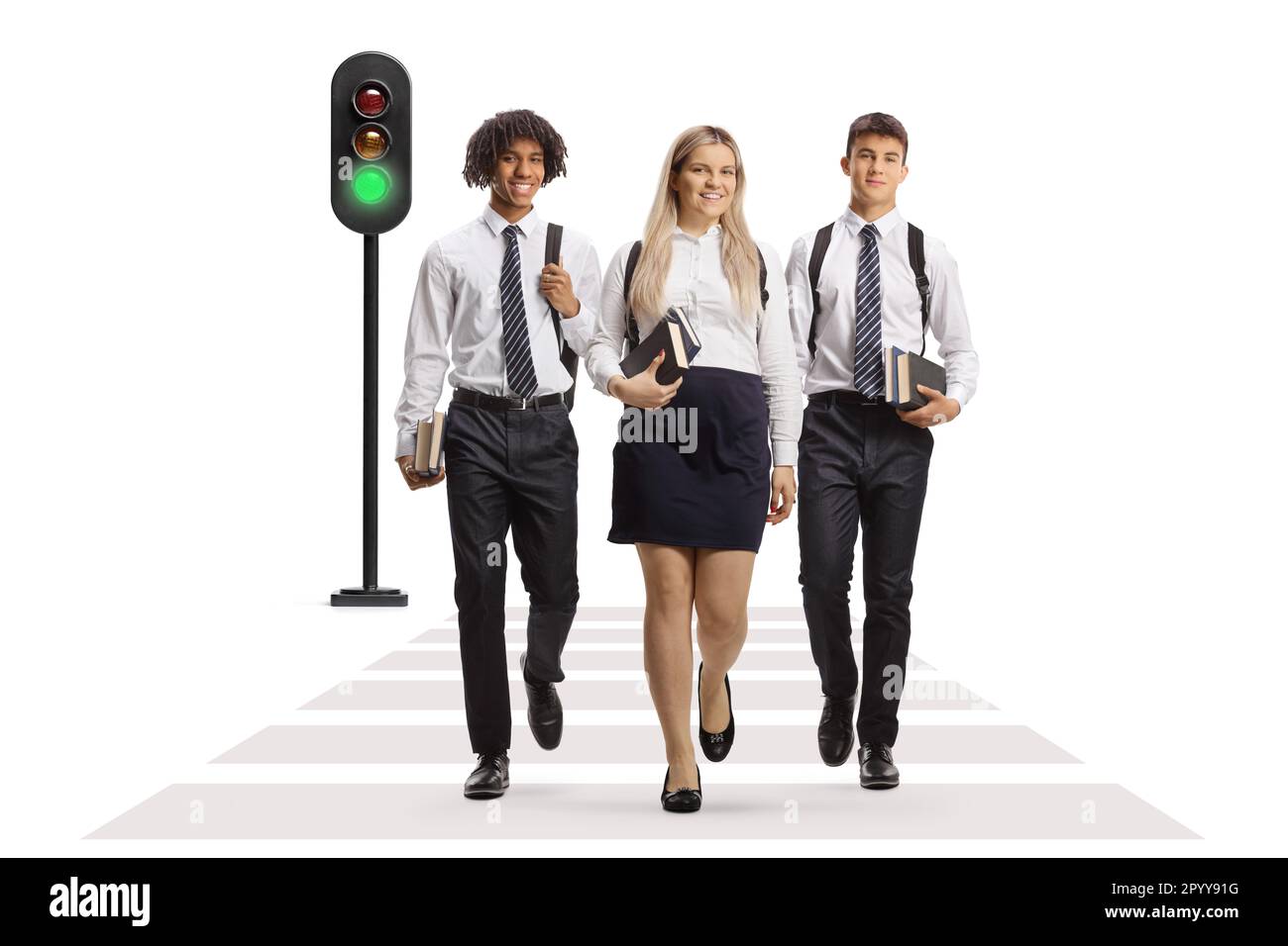 Full length portrait of a group of college students carrying books and crossing street at green traffic light isolated on white background Stock Photo