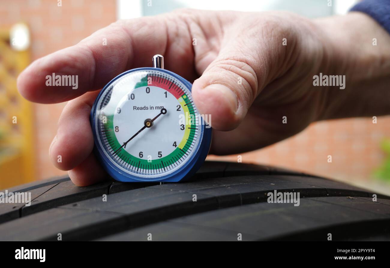 The hand of a man is measuring the tread depth of a car tire in mm. He