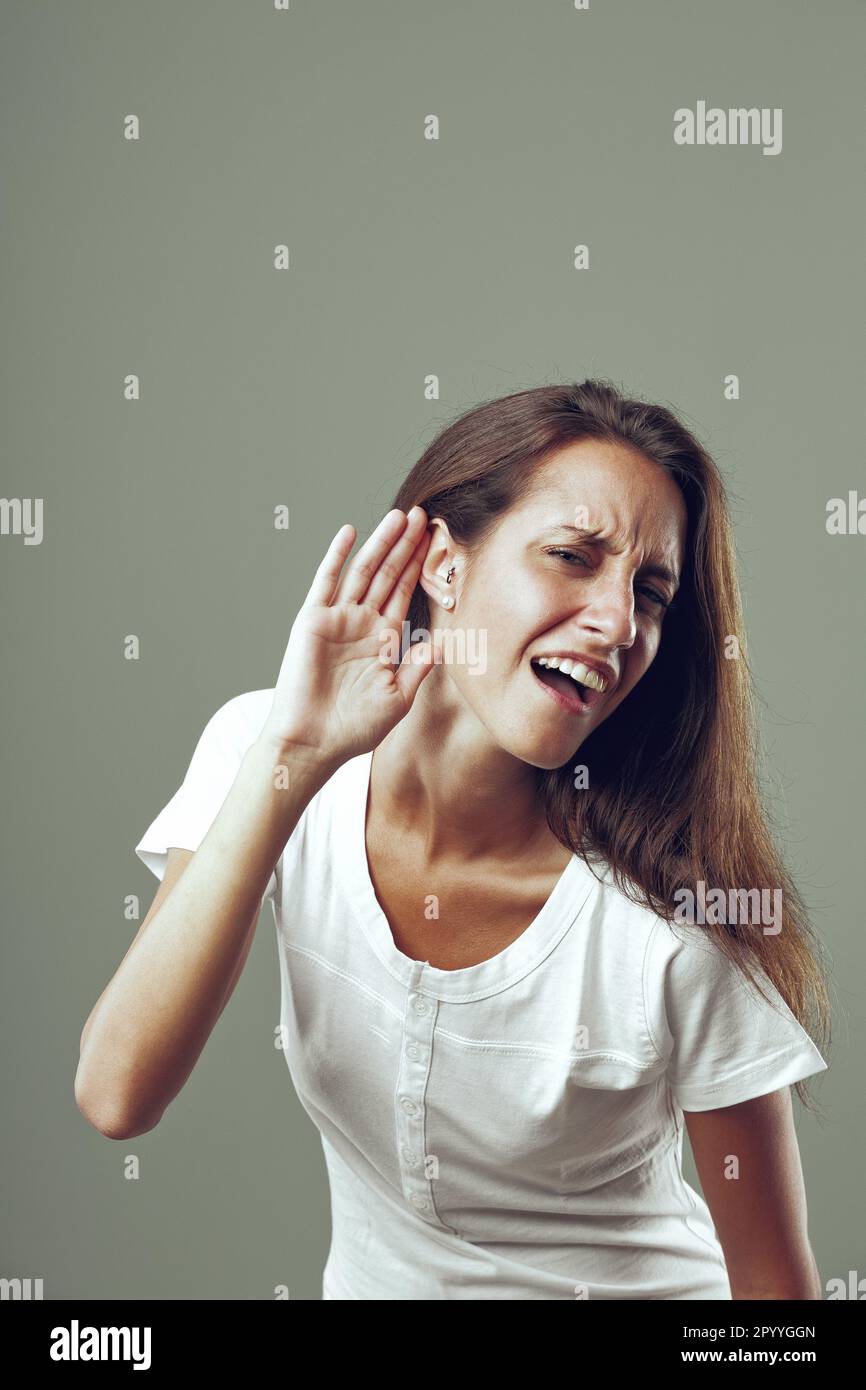 'What did you say? I can't hear you!' seems to be the meaning behind young woman's hand to ear gesture and annoyed expression. Beautiful, slim, long-h Stock Photo