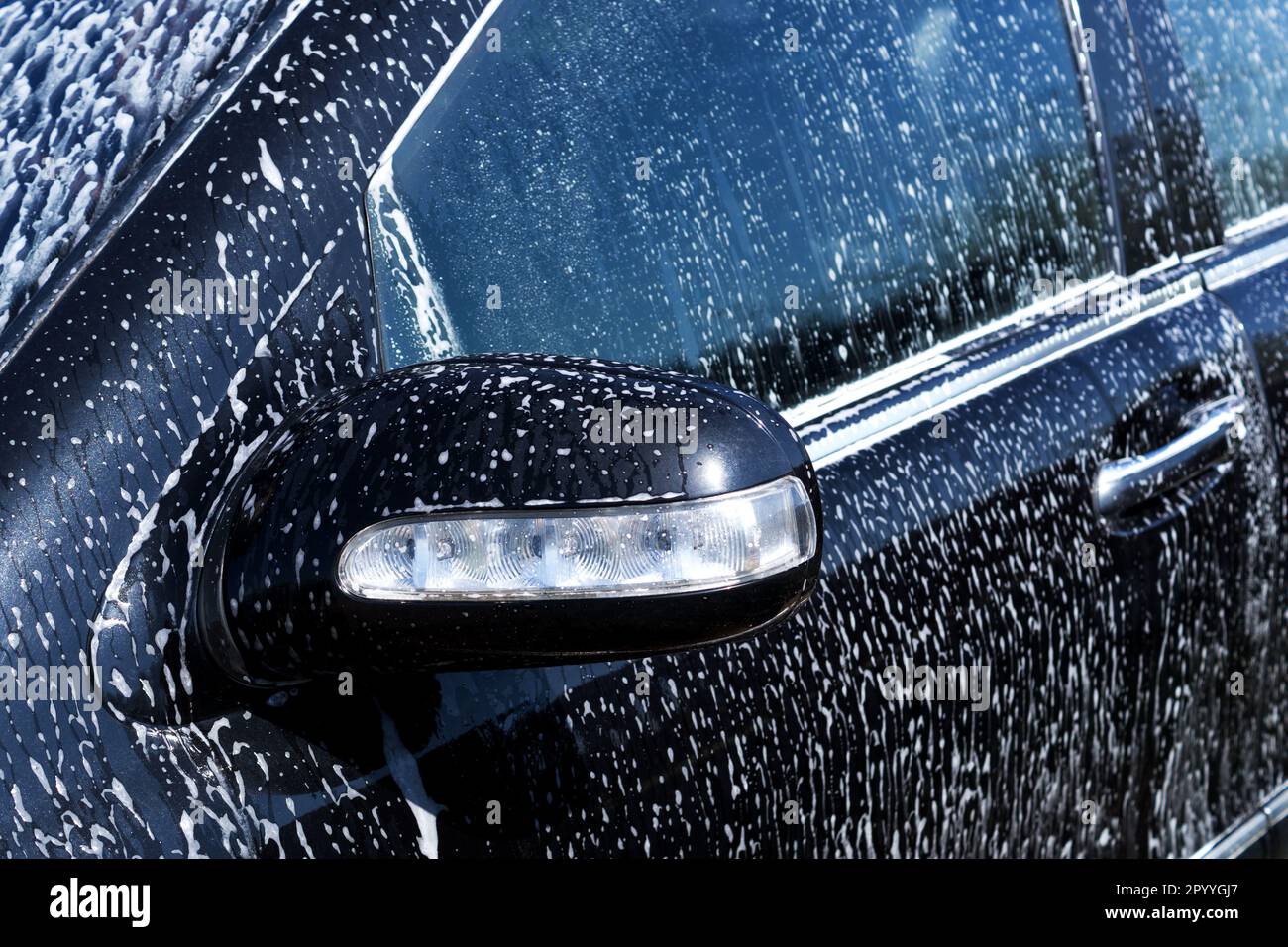 Washing black car with white soap foam. Cleaning auto, car wash, auto care. Rearview mirror wirh turn signal close up Stock Photo