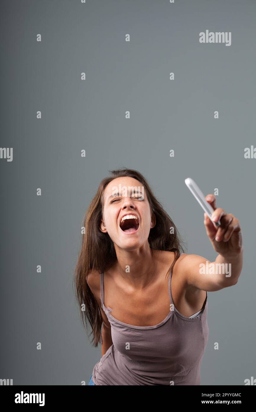 With an athletic leap, a woman throws her cell phone away. Revitalized by anger, she has violent strength and accompanies the gesture with a furious s Stock Photo