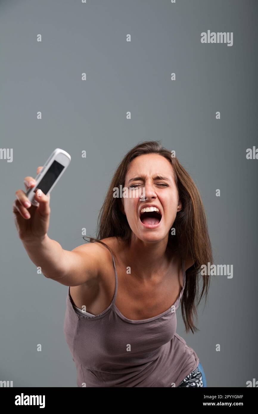 Athletically hurling her cellphone, the woman unleashes her anger-fueled violent strength, accompanied by a furious scream. She's completely fed up! Stock Photo