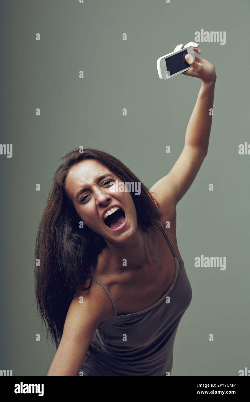 Angry girl throws her cellphone with rage. Emotional portrait of a young woman isolated on a neutral background. She thinks, 'I'm fed up with this sma Stock Photo