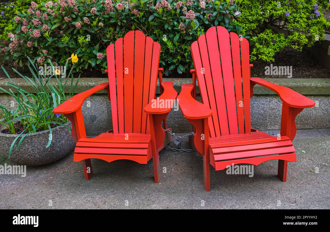 Red Adirondack chair setting at the garden. Traditional curveback red wooden beach chair, outdoor patio adirondack chairs with contoured backs Stock Photo