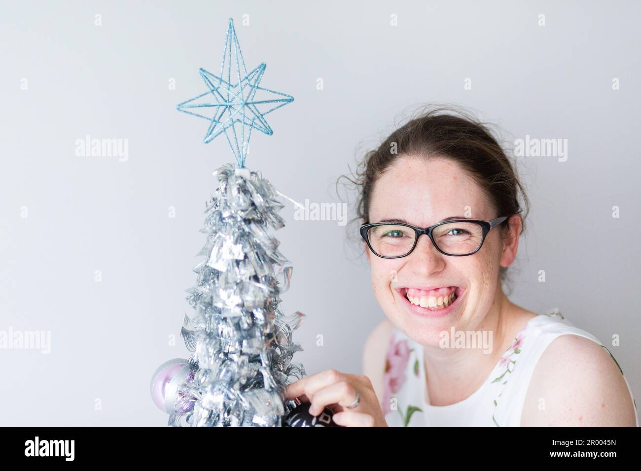 Smiling woman by mini silver Christmas tree indoors Stock Photo