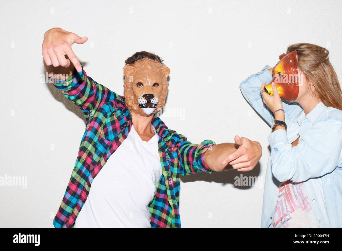 Embracing their wild side. Young hipster guy wearing a lion mask and gesturing alongside a young woman wearing a bear mask. Stock Photo