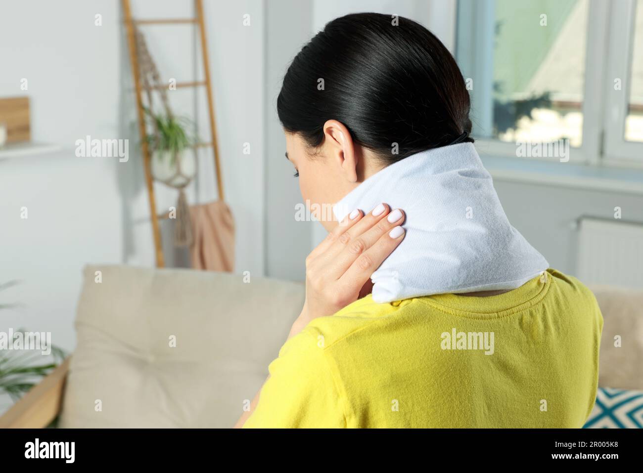 Woman using heating pad on neck at home Stock Photo