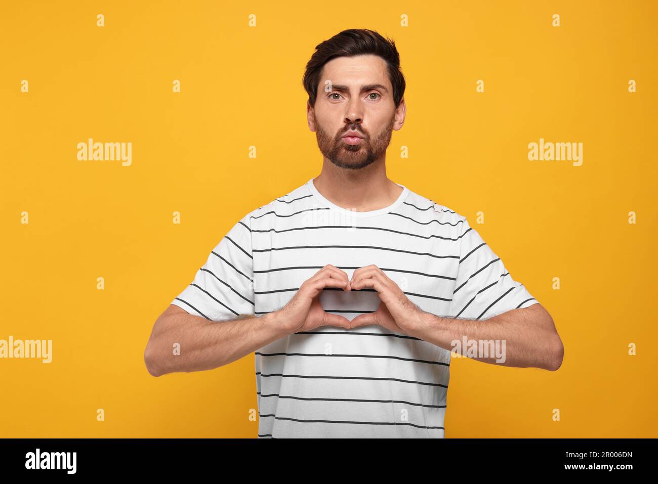 Handsome man making heart with hands and blowing kiss on orange ...
