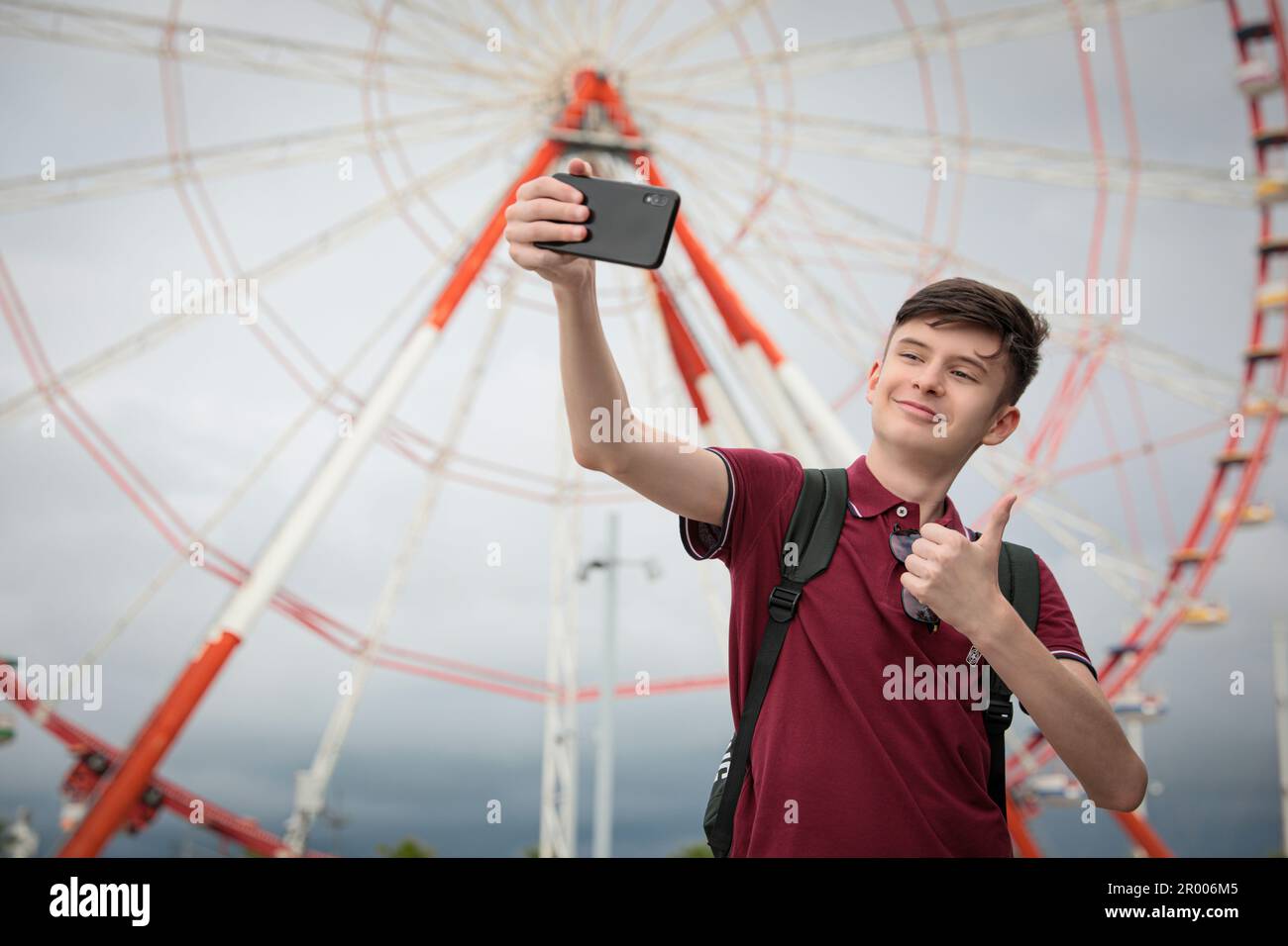 Teenage boy taking selfie near Ferris wheel outdoors. Space for text Stock Photo