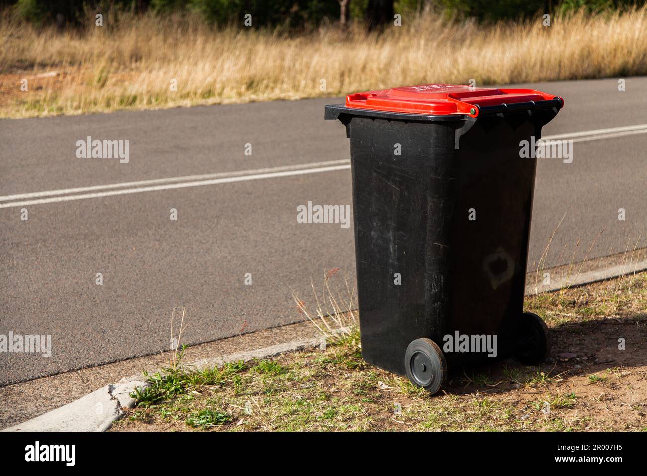Red council garbage bin beside road awaiting collection Stock Photo Alamy